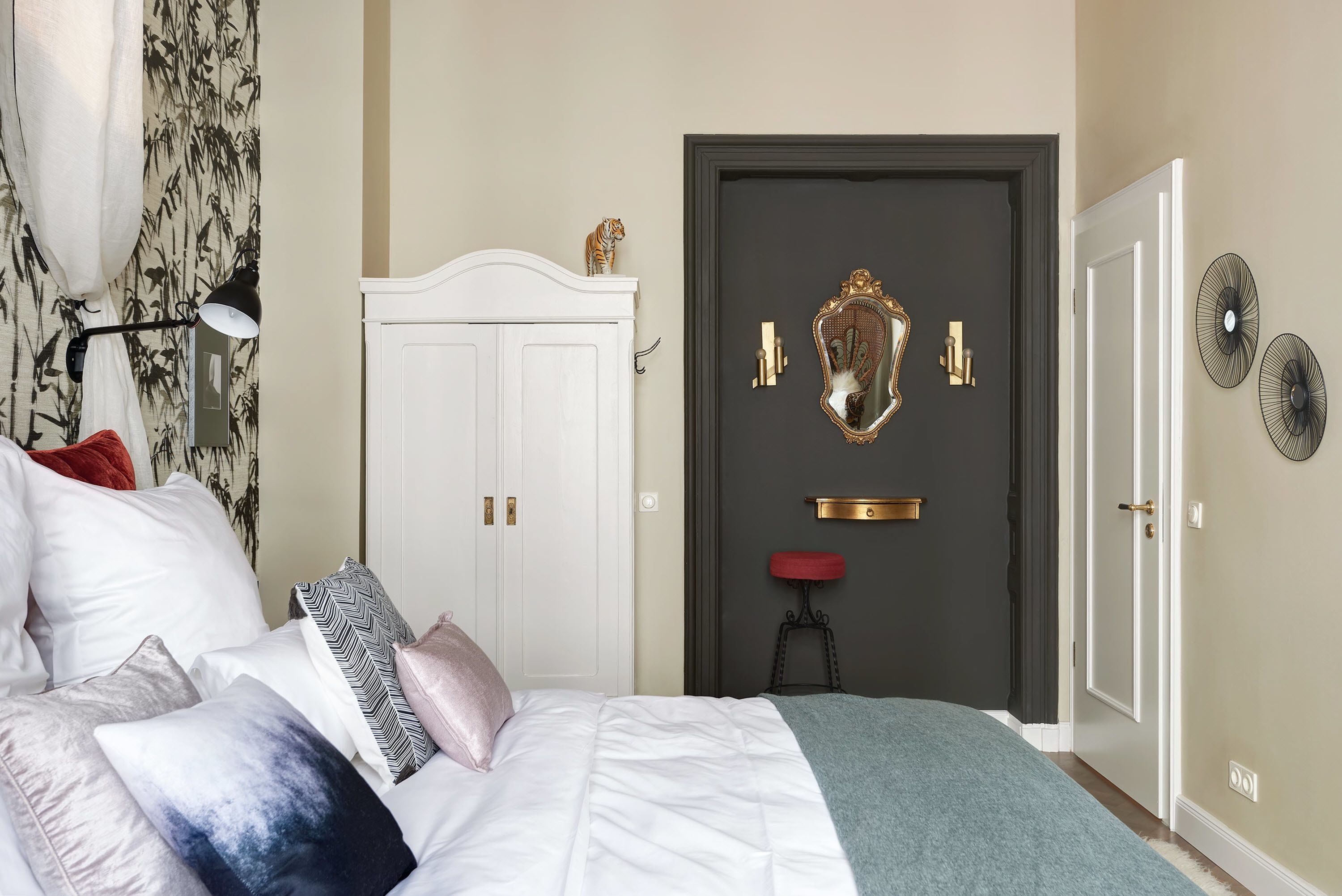 Un dormitorio con una cama, un armario blanco, una puerta con espejo y un taburete rojo.