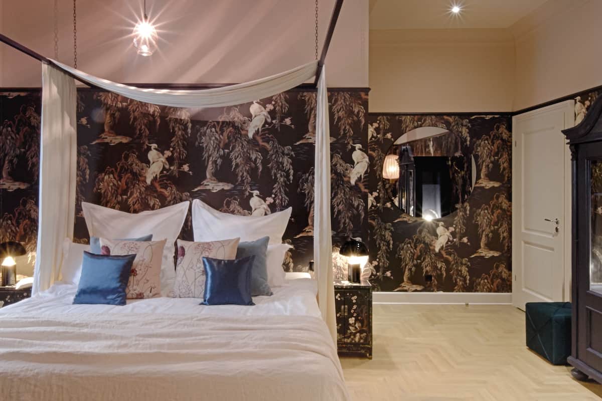 A bedroom with a canopy bed, floral wallpaper, and a nightstand with a lamp.