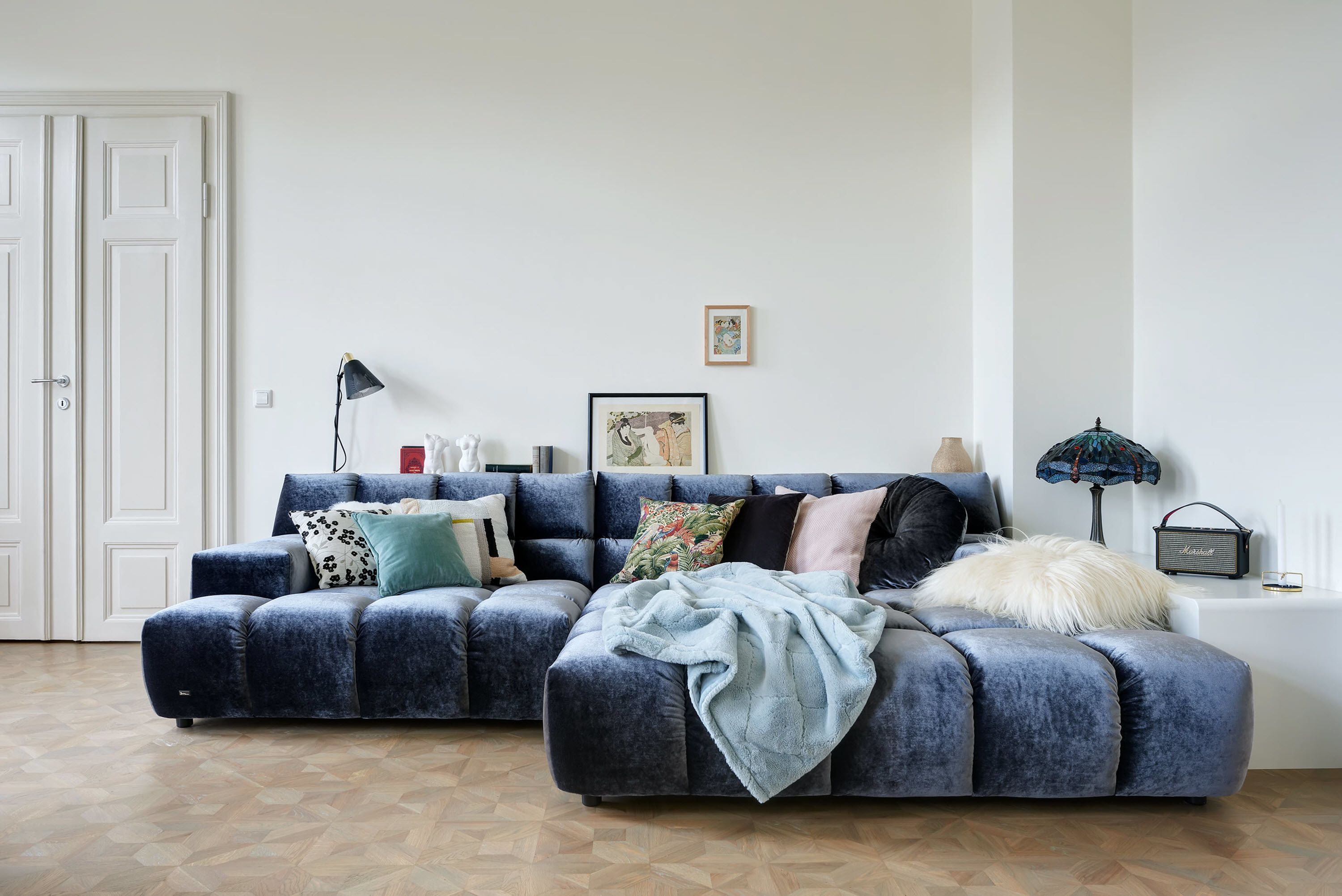 Un salon moderne avec un canapé d’angle, une lampe et un tableau encadré au mur.