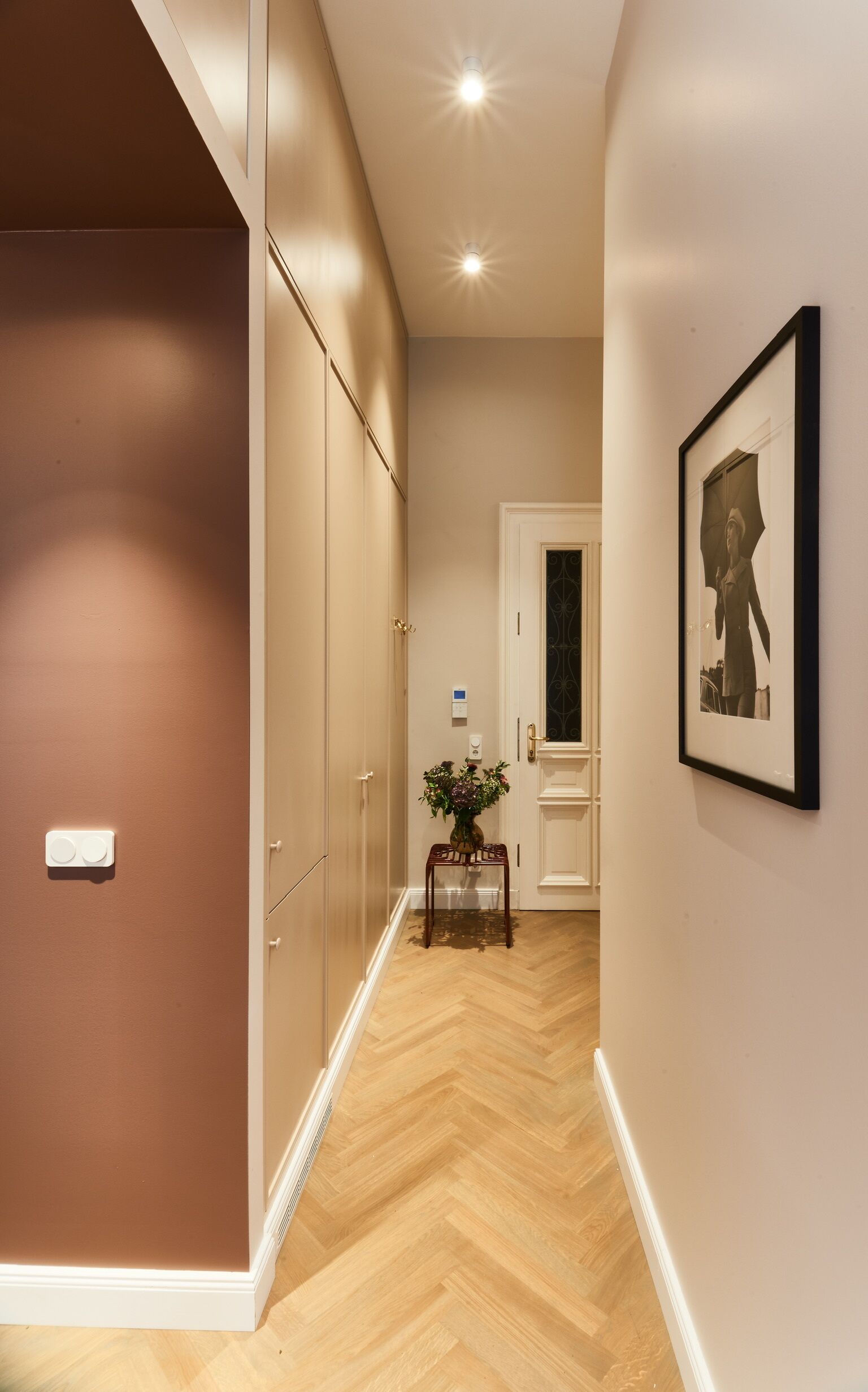 A hallway with a wooden herringbone floor, a white door, and a framed picture on the wall.