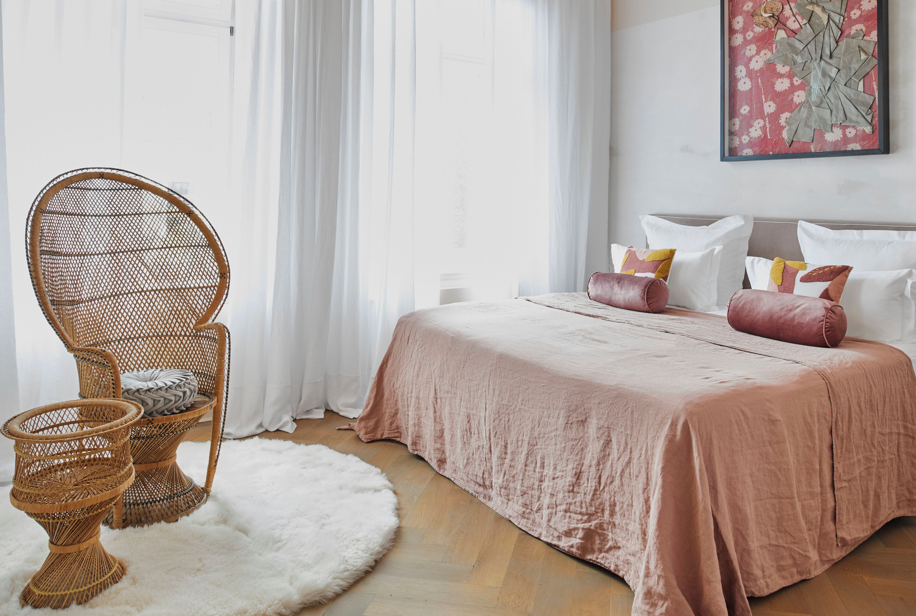 A bedroom with a bed, a wicker chair, and a white furry rug.