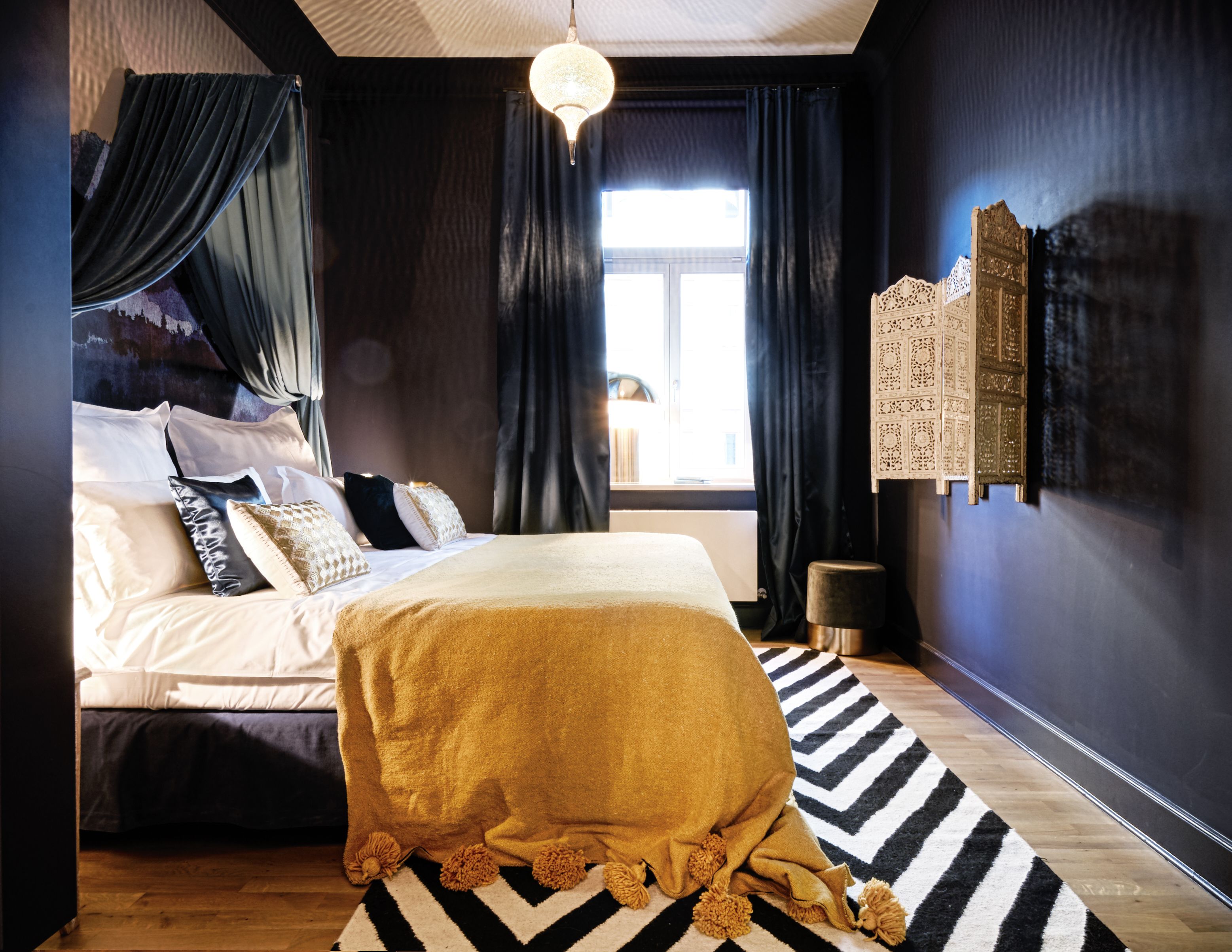 A bedroom with a bed, a window, a decorative wall piece, and a rug.