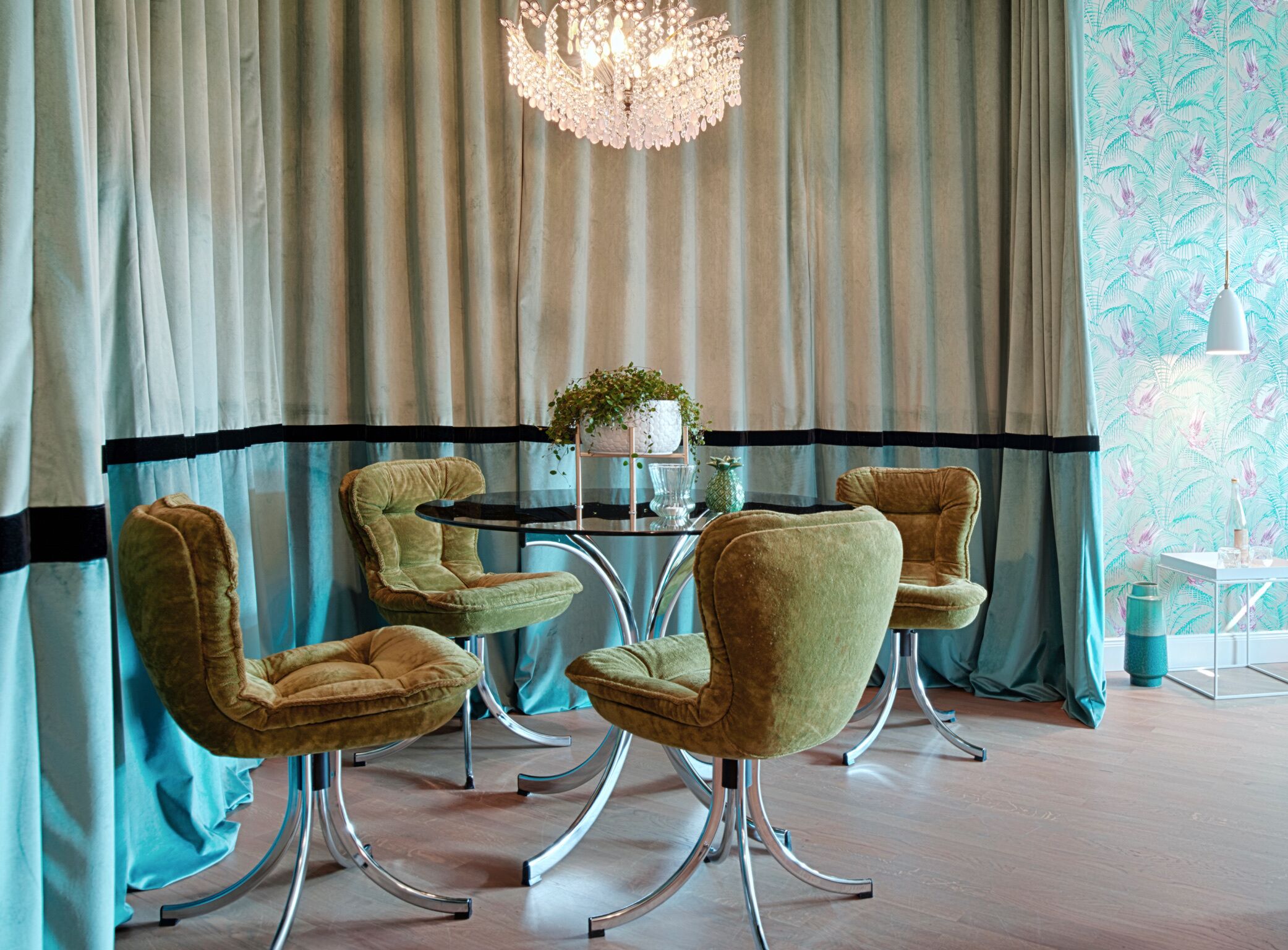 A dining area with a round table, four chairs, a chandelier, and a patterned wall.