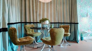 A dining area with a round table, four chairs, a chandelier, and a patterned wall.