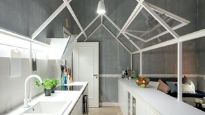 Et moderne køkken med en hvid bordplade, vask og bagvæg. Der står plantekasser på bordet og en skål med frugt.