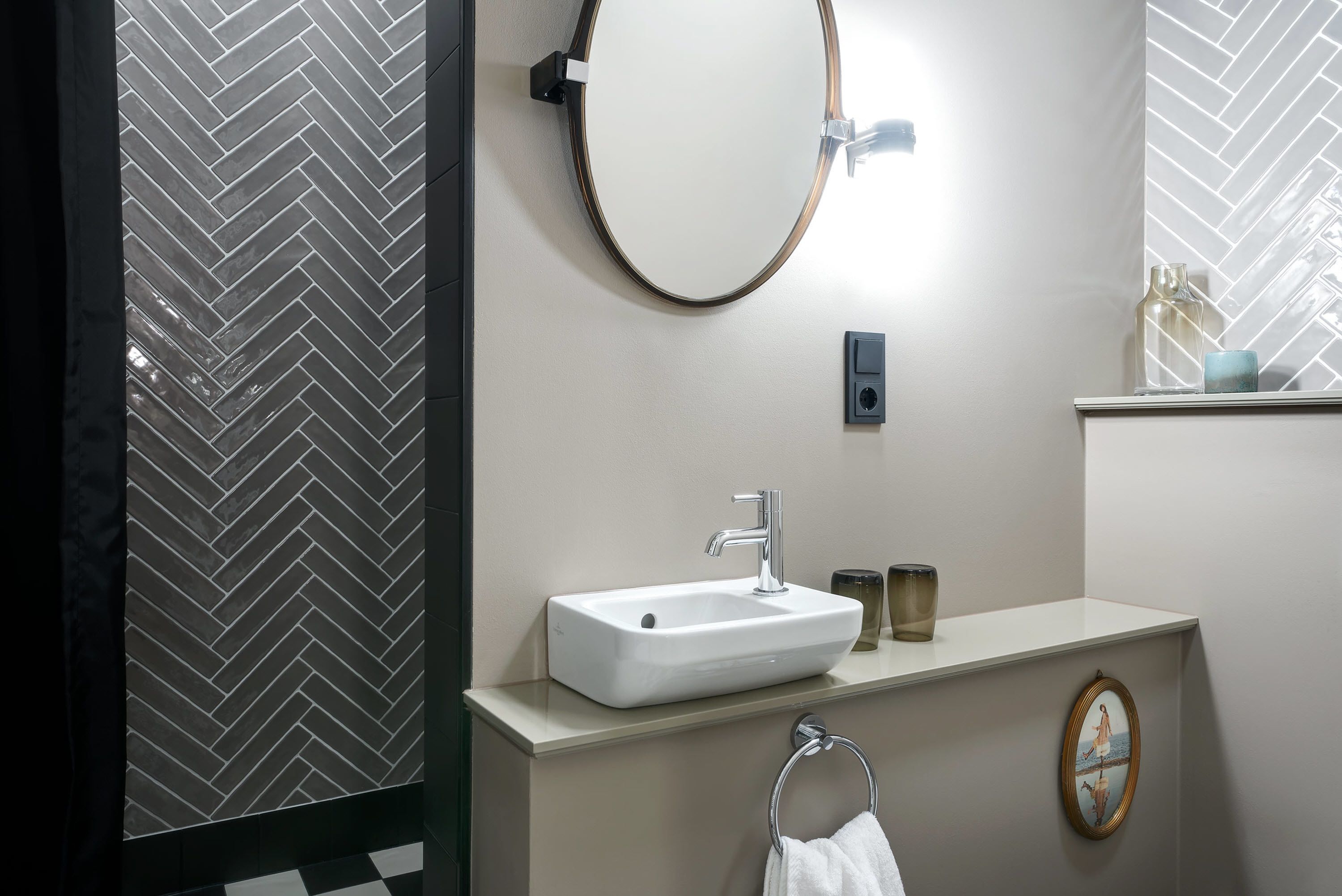 Un baño moderno con un lavamanos blanco, un espejo redondo y un aro para toallas.