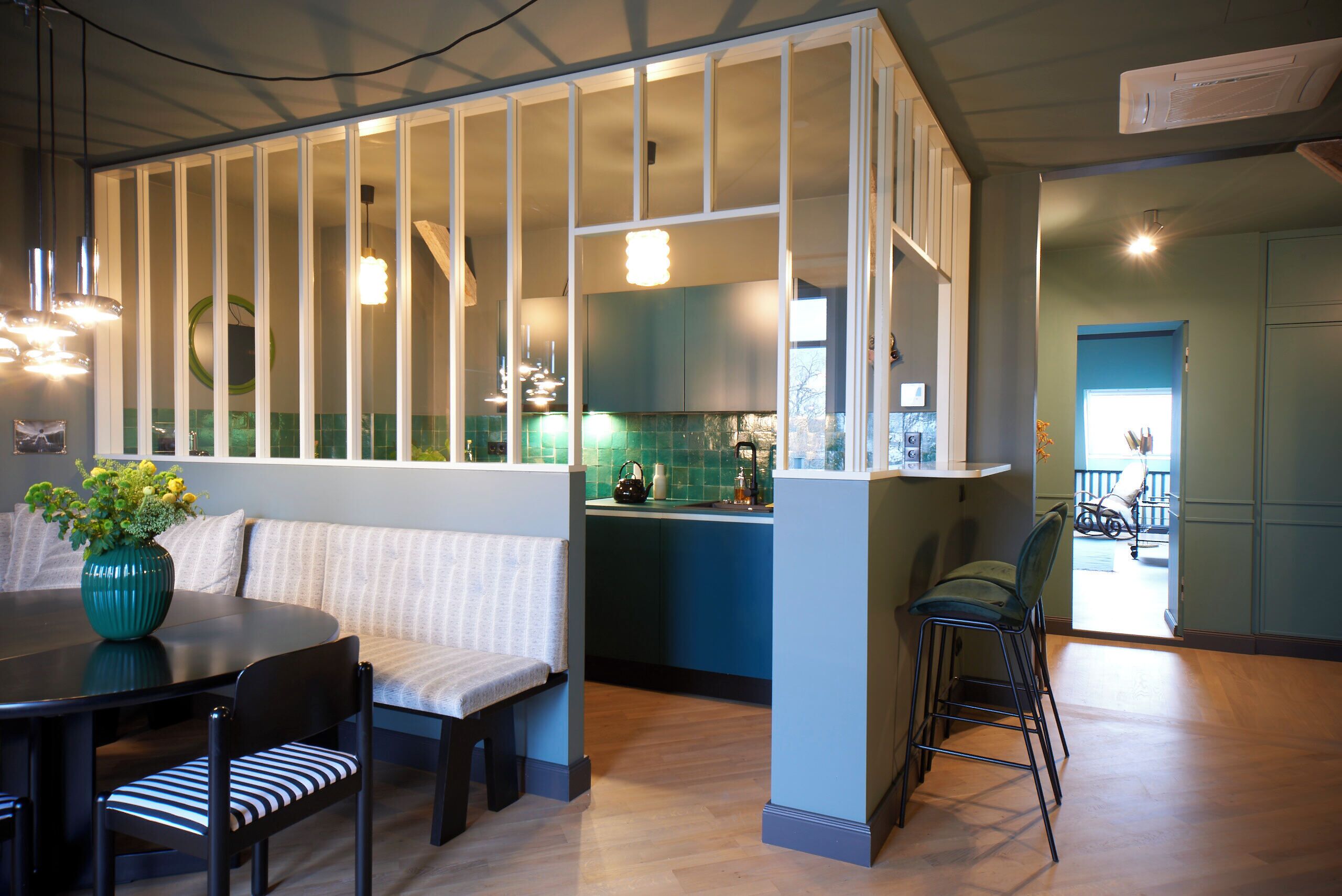 Eine moderne Küche mit blauer Arbeitsplatte, ein Essbereich mit rundem Tisch und gestreiften Stühlen sowie eine Sitzecke mit einer Bank.