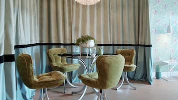A dining area with a round table, four chairs, a chandelier, and a patterned wallpaper.