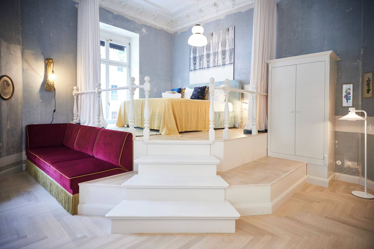 A bedroom with a bed, a red sofa, a staircase, and a wardrobe.