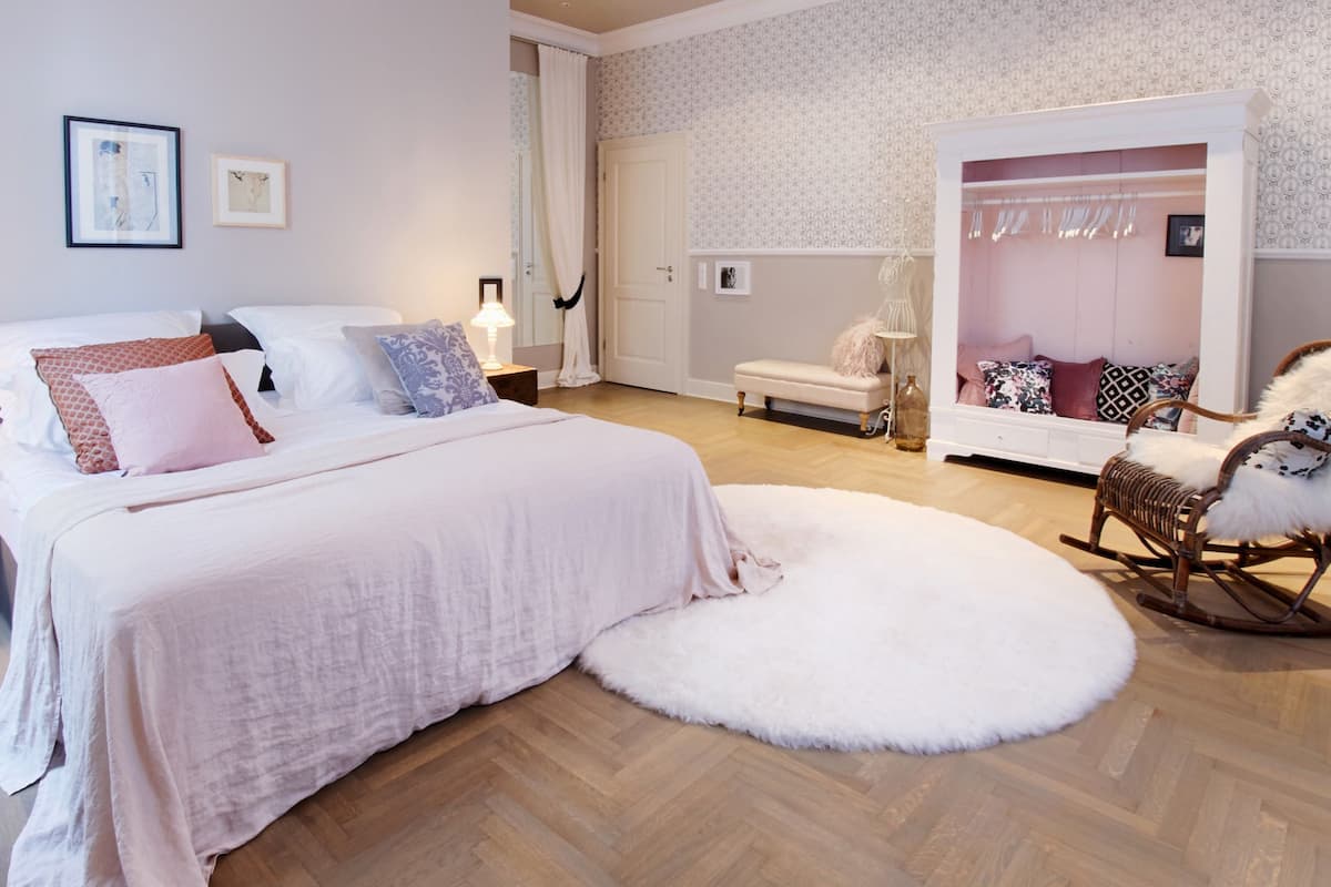 A bedroom with a large bed, a white fluffy rug, a rocking chair, and a wardrobe.