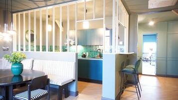Une cuisine moderne avec des meubles bleus, un coin repas avec une table ronde et des chaises à rayures, et une vue sur l’extérieur.