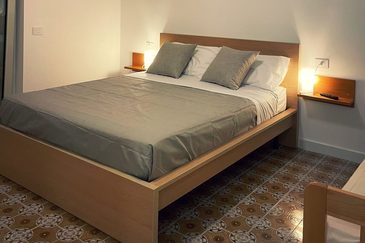 A single bed with a wooden frame, grey bedding, and two bedside lamps.