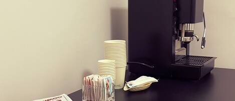 A coffee machine, stacks of white cups, and a tray with coffee packets on a black table.
