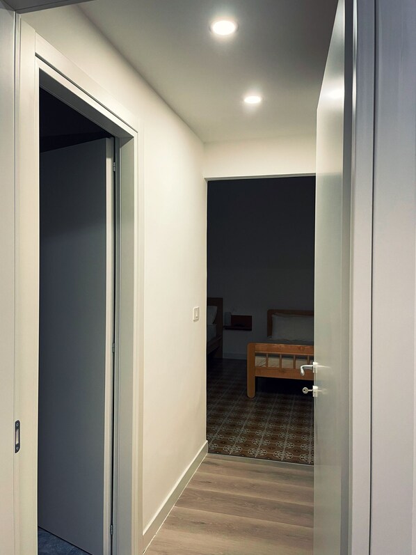 A narrow hallway leading to a bedroom with a bed, a nightstand, and a wall-mounted shelf. - B&B La Ginestra (Torre del Greco)