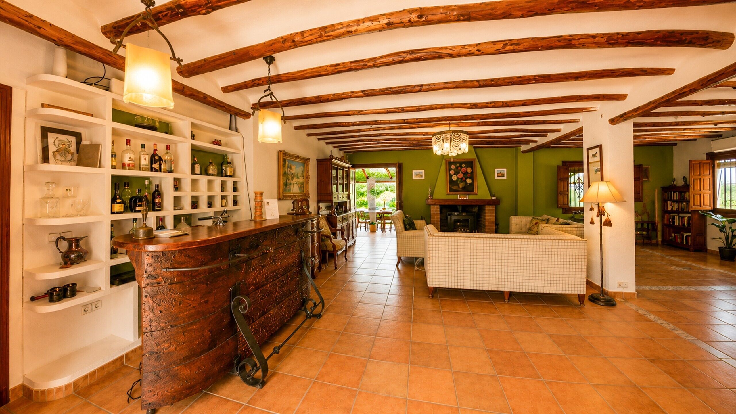 Una habitación amplia con techo de madera, una zona de bar con estantes y un área de estar con chimenea.