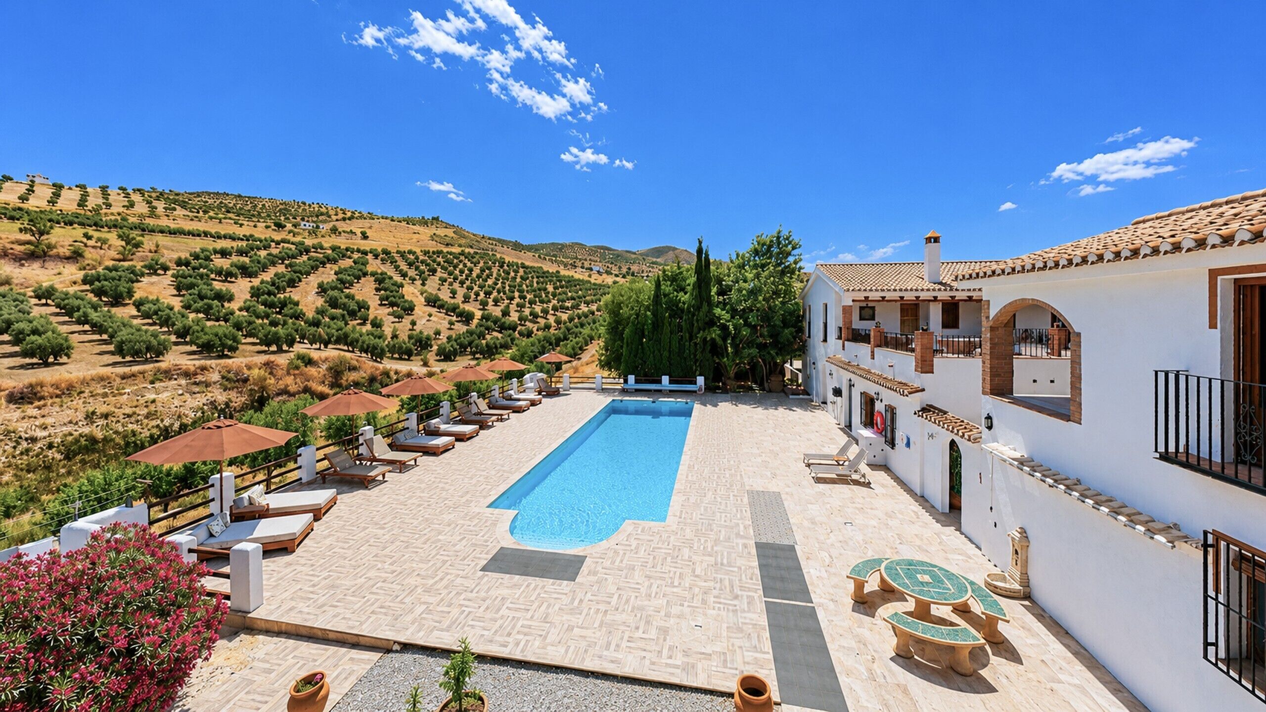 A pool area with lounge chairs and umbrellas, surrounded by a hilly landscape.