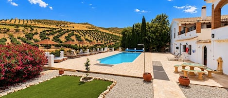 A pool area with a view of a hilly landscape, outdoor seating, and a building with a tiled roof.