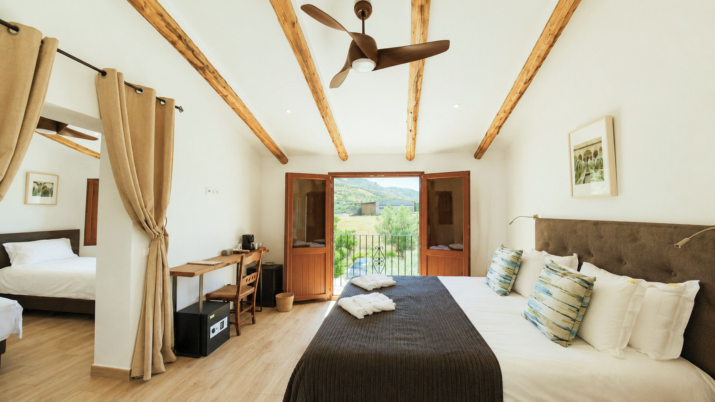 Un dormitorio con cama, escritorio, silla, ventilador de techo y vistas al exterior.