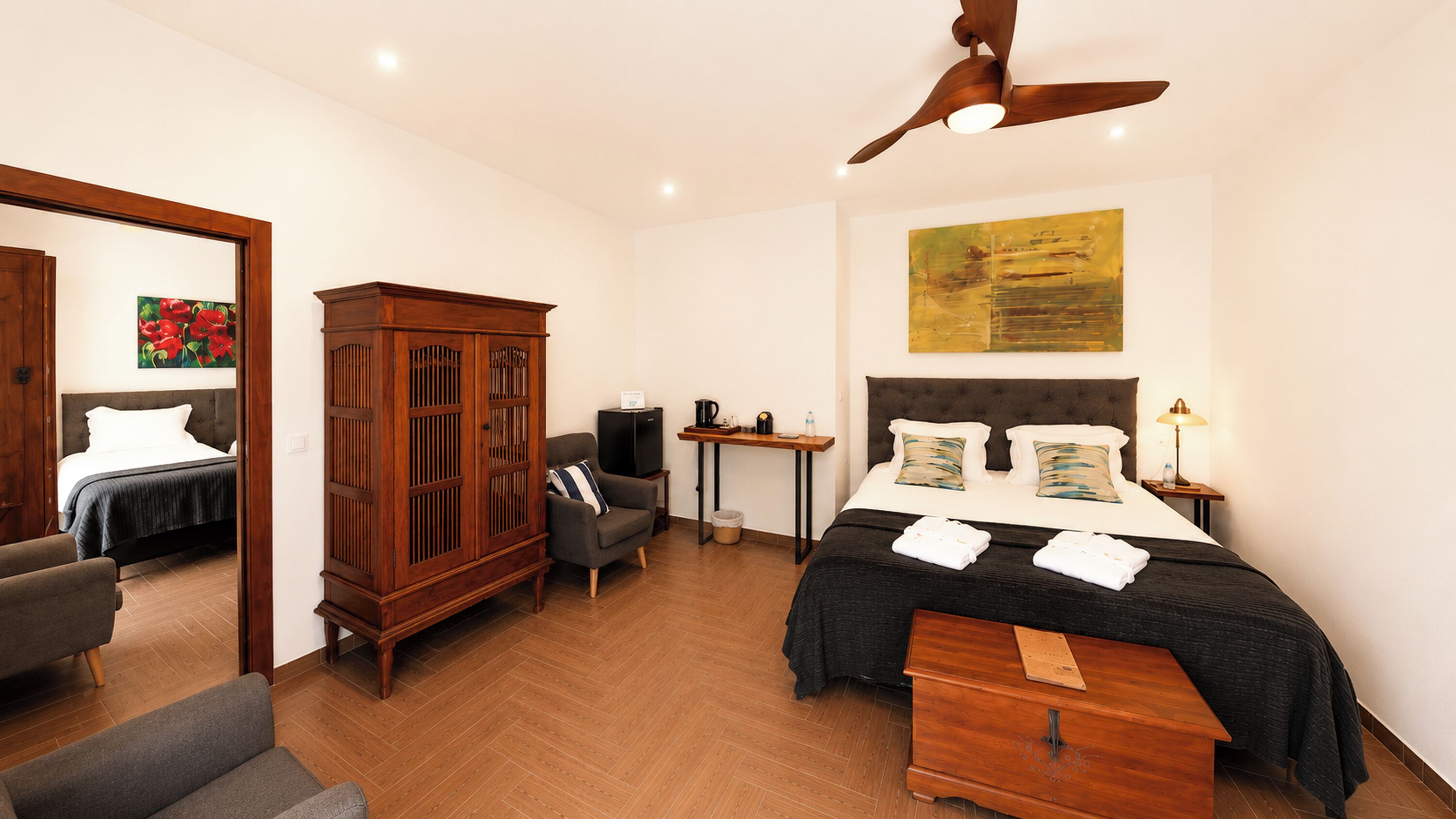 Quarto de hotel com cama, escrivaninha, guarda-roupa, cadeira e ventoinha no teto.