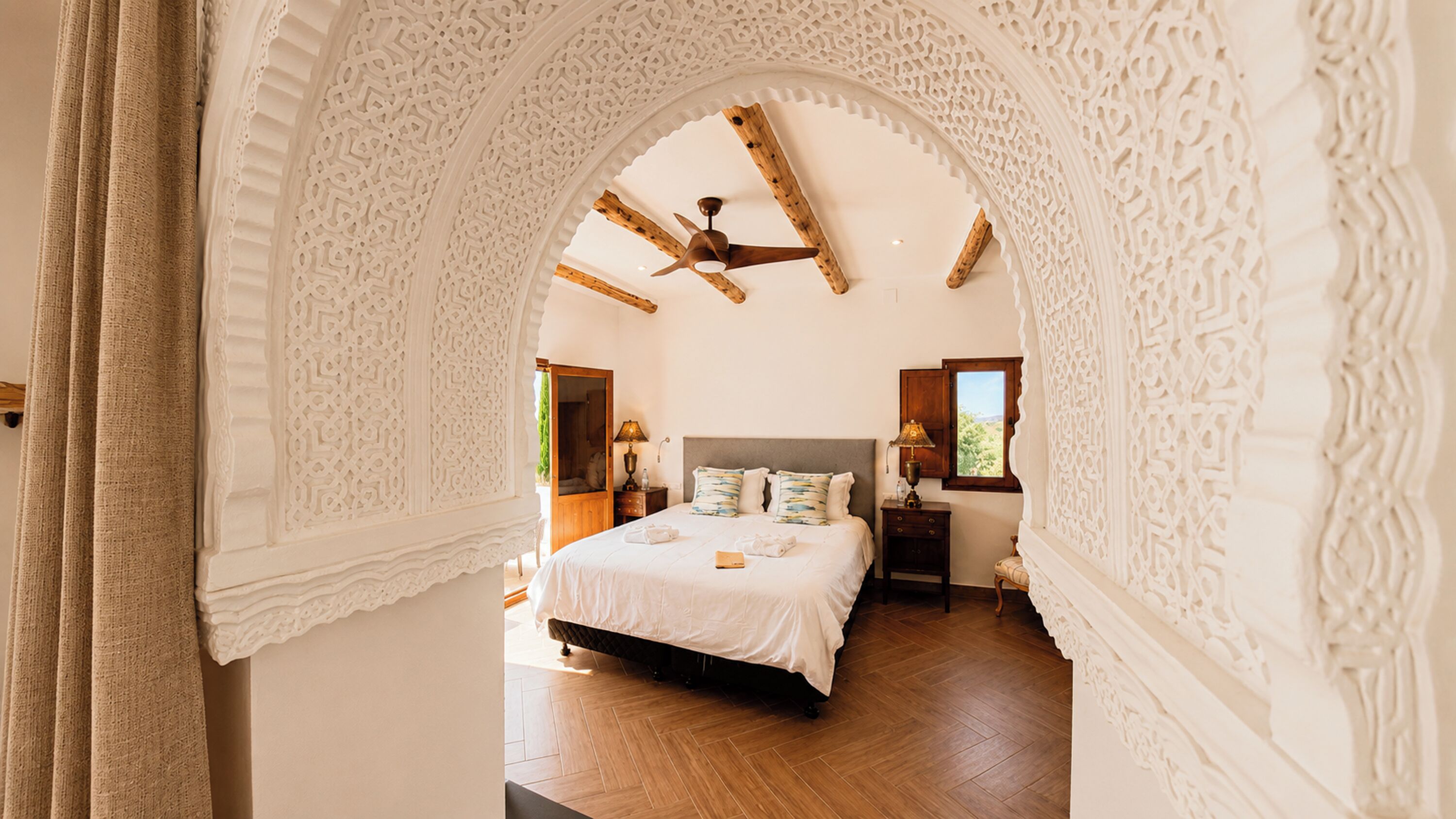 A bedroom with a bed, a nightstand, a lamp, and a window.