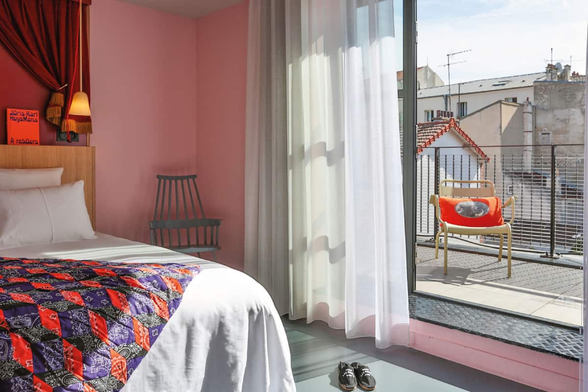 Un dormitorio con cama, una silla, una ventana con cortinas y vistas al exterior.