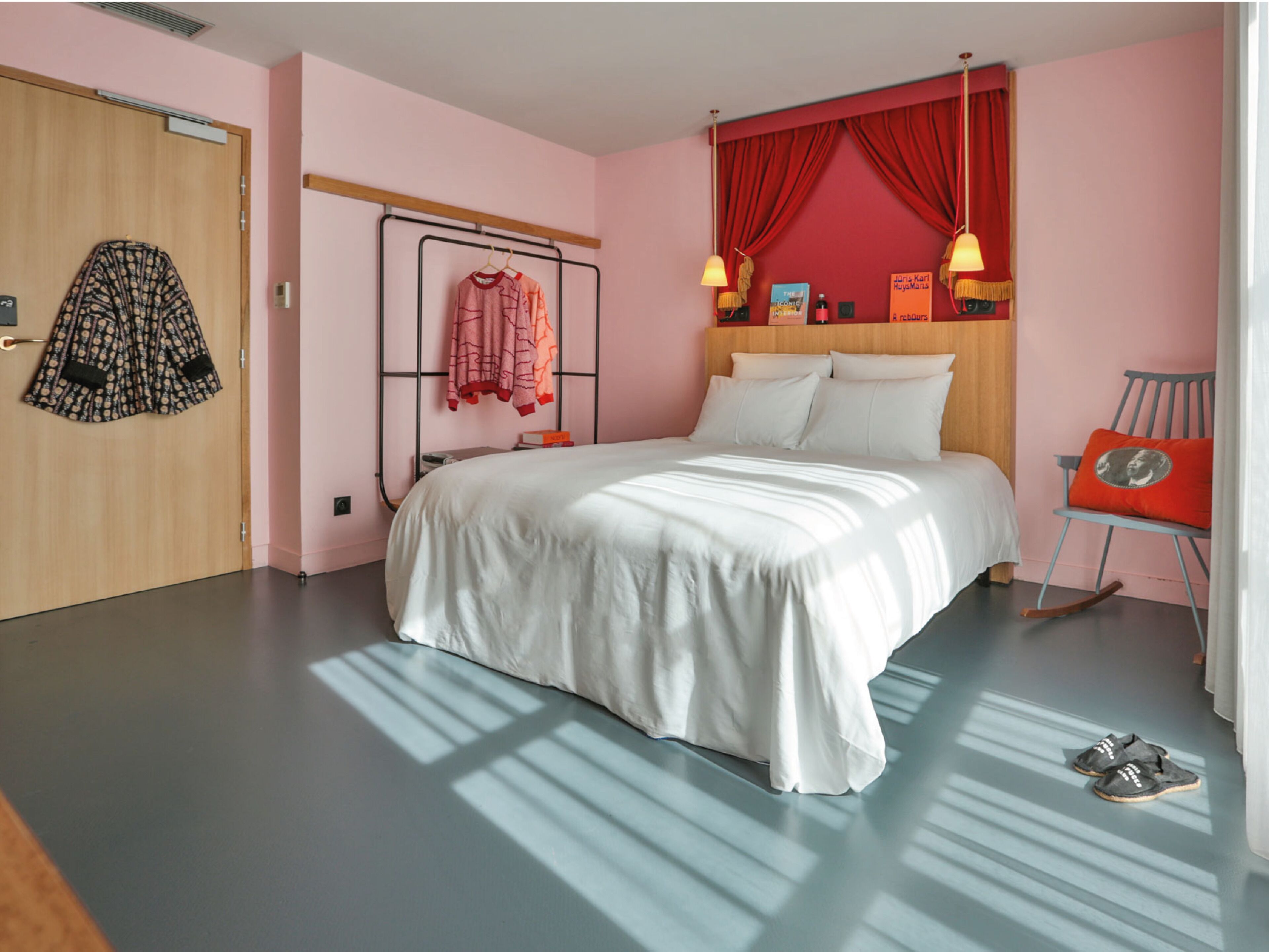 A bedroom with a bed, a hanging chair, a wardrobe, and a shelf with books and a lamp.