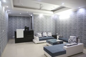 A modern living room with a reception desk, sofas, and a coffee table. - Mint City Center Suites (Noida)