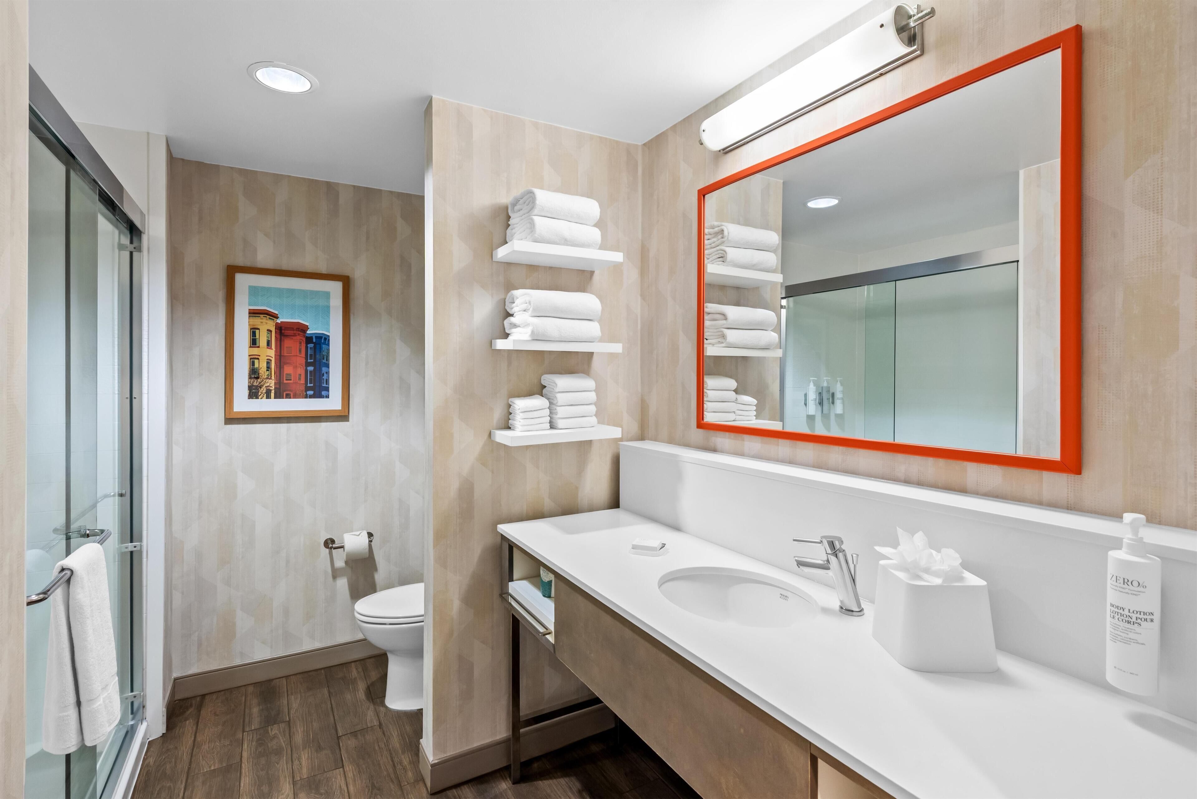 A modern bathroom with a glass shower enclosure, a toilet, a sink with a mirror, and towel racks.