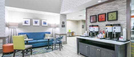 A modern hotel lobby with a blue sofa, a coffee station, and a breakfast area.