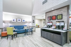 A modern hotel lobby with a blue sofa, a coffee station, and a breakfast area.