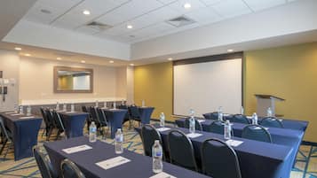 A conference room with tables, chairs, water bottles, a projector, and a screen.