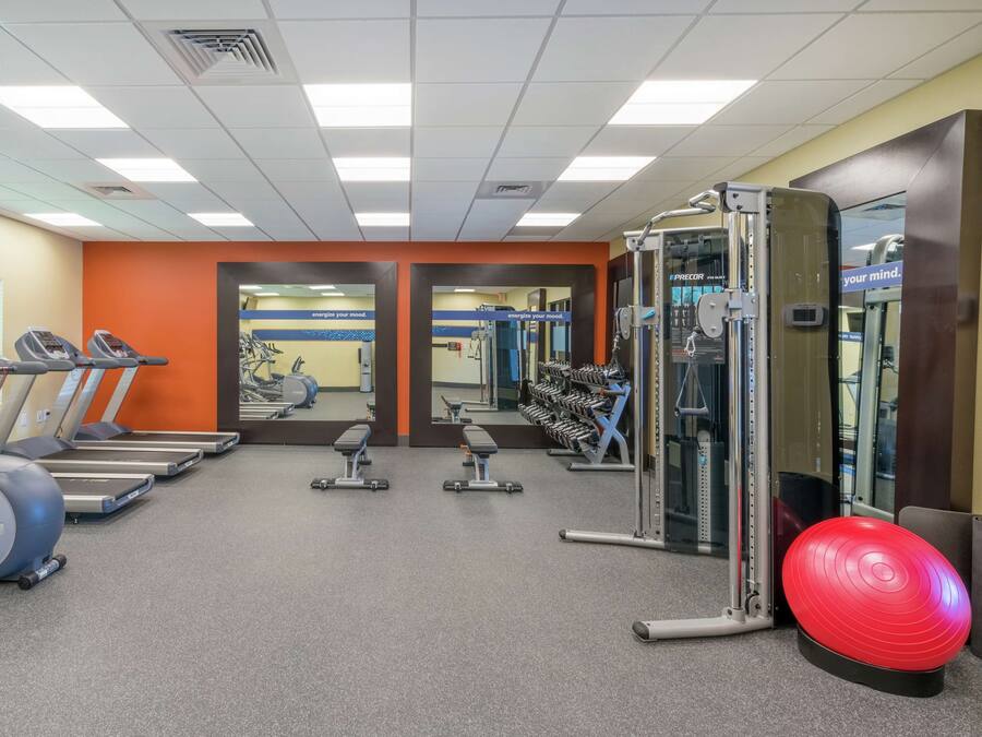 Un gimnasio con cintas de correr, elípticas, bancos de pesas y una pelota de ejercicios roja.