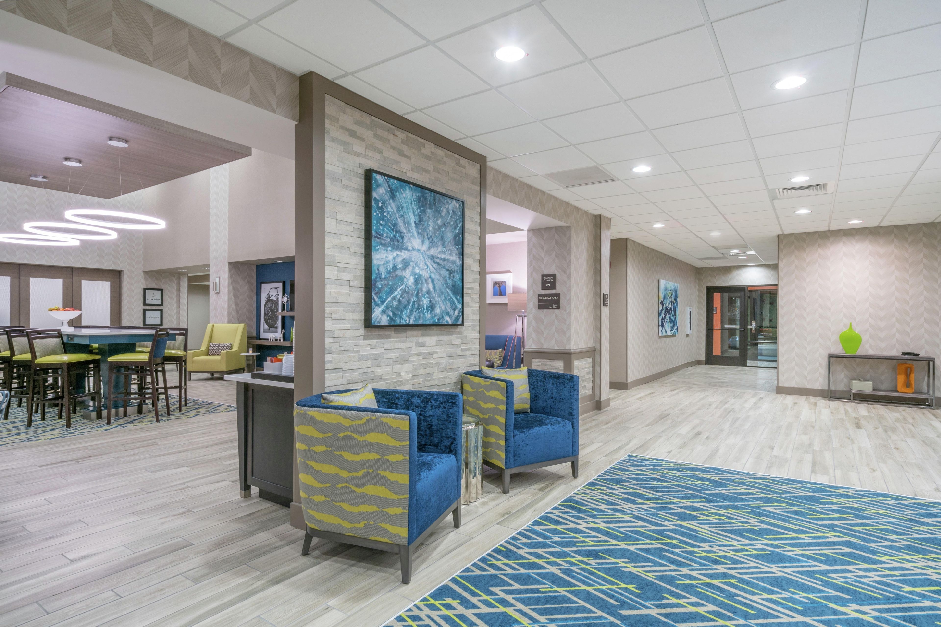A hotel lobby with seating areas, a reception desk, and a large abstract painting on the wall.