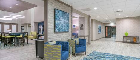 A hotel lobby with seating areas, a reception desk, and a large abstract painting on the wall.