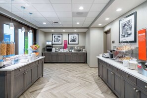 A modern kitchen area with a herringbone floor pattern, equipped with various appliances and food dispensers. - Hampton Inn & Suites Glenarden/Washington DC (Lanham)