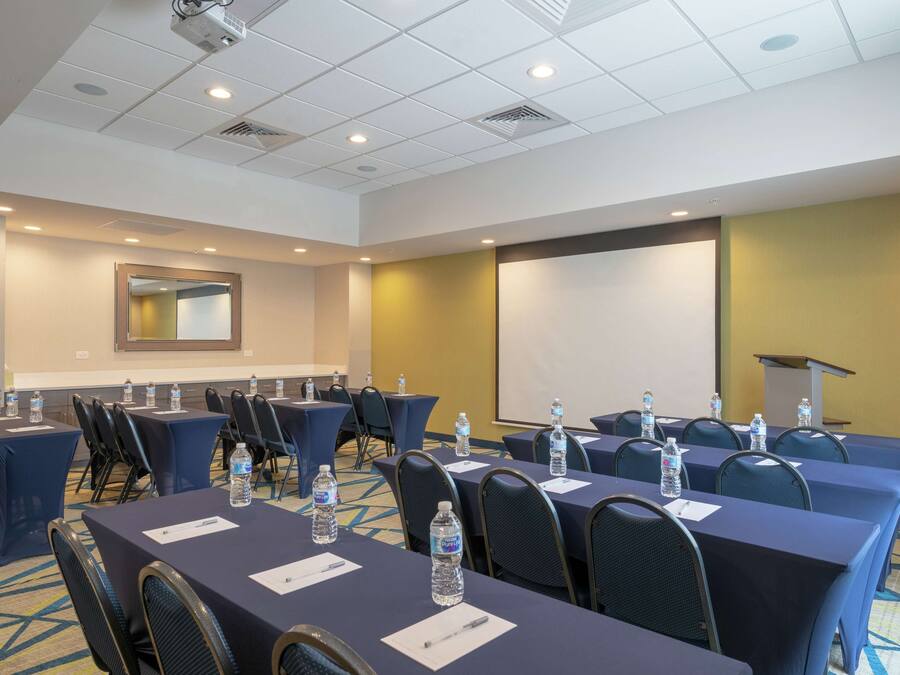 A conference room with tables, chairs, water bottles, and a projector screen.
