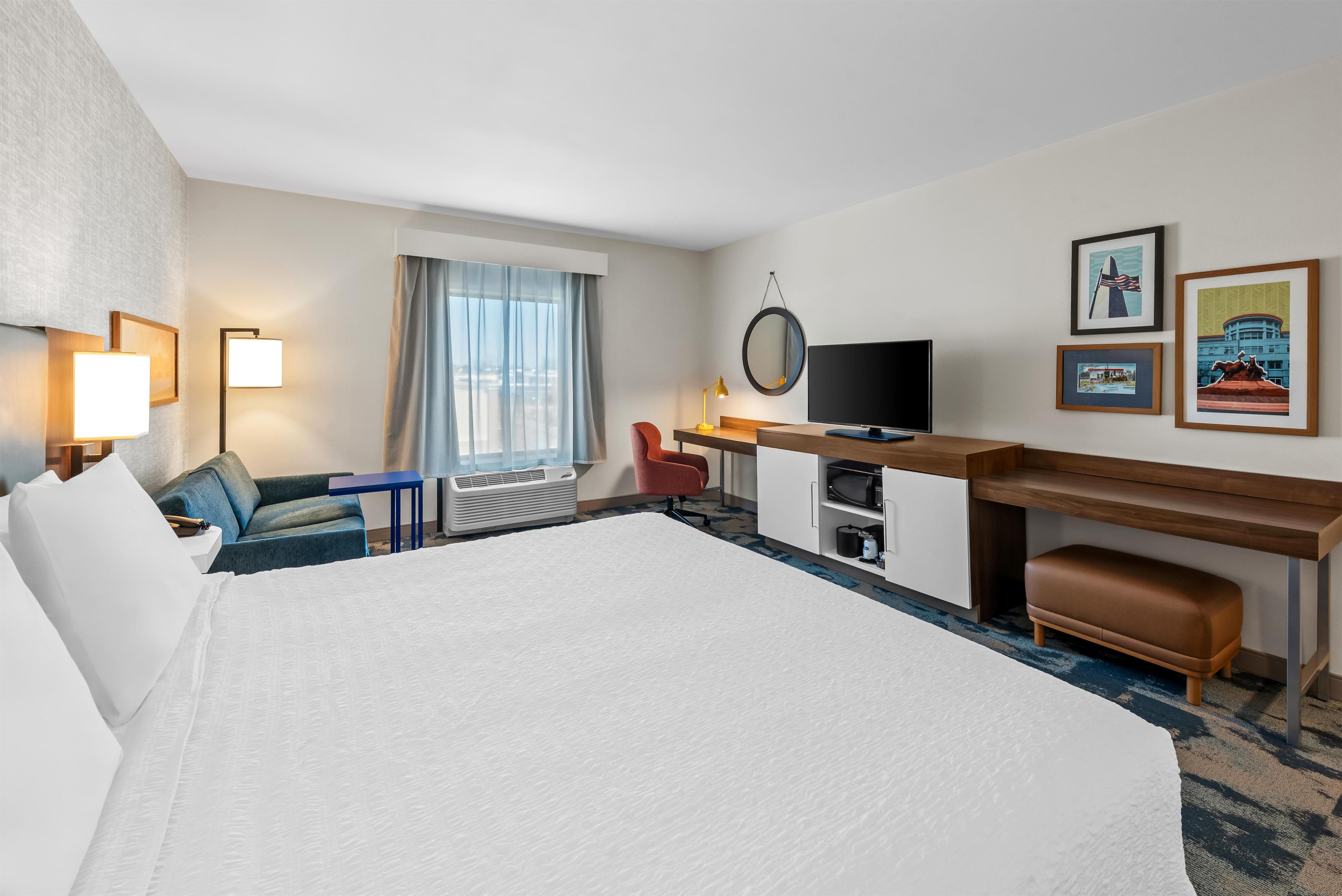 A hotel room with a large bed, a desk with a computer, a chair, a TV, and a window with curtains.