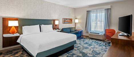 Quarto de hotel com cama grande, escrivaninha, cadeira, televisão e janela com cortinas.