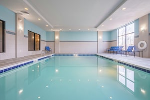 Una piscina con agua cristalina, rodeada de sillas azules y un flotador a la derecha.