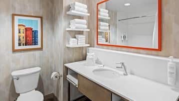 A modern bathroom with a toilet, sink, and mirror. There are white shelves with towels and a framed picture on the wall.
