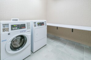 A commercial washer and dryer unit with control panels, located in a room with tiled flooring and a white wall. - Hampton Inn & Suites Glenarden/Washington DC (Lanham)