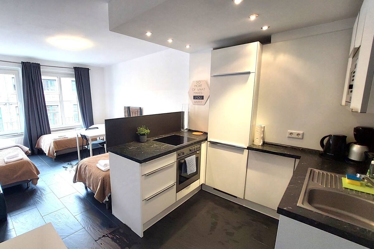 Une chambre d’hôtel compacte comprenant un coin cuisine, deux lits simples, une petite table et une fenêtre avec des rideaux.