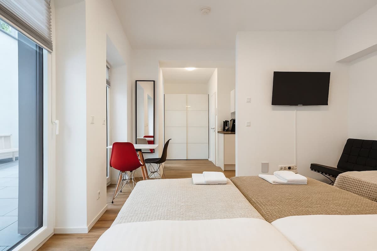 Une chambre d’hôtel moderne avec deux lits, un bureau, une chaise rouge, une télévision et une grande fenêtre.
