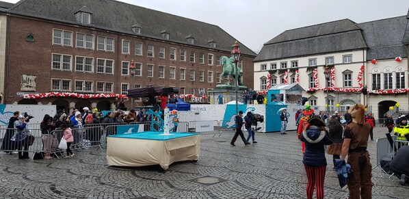 A public square with a fountain, a statue, and buildings with red and white decorations.
