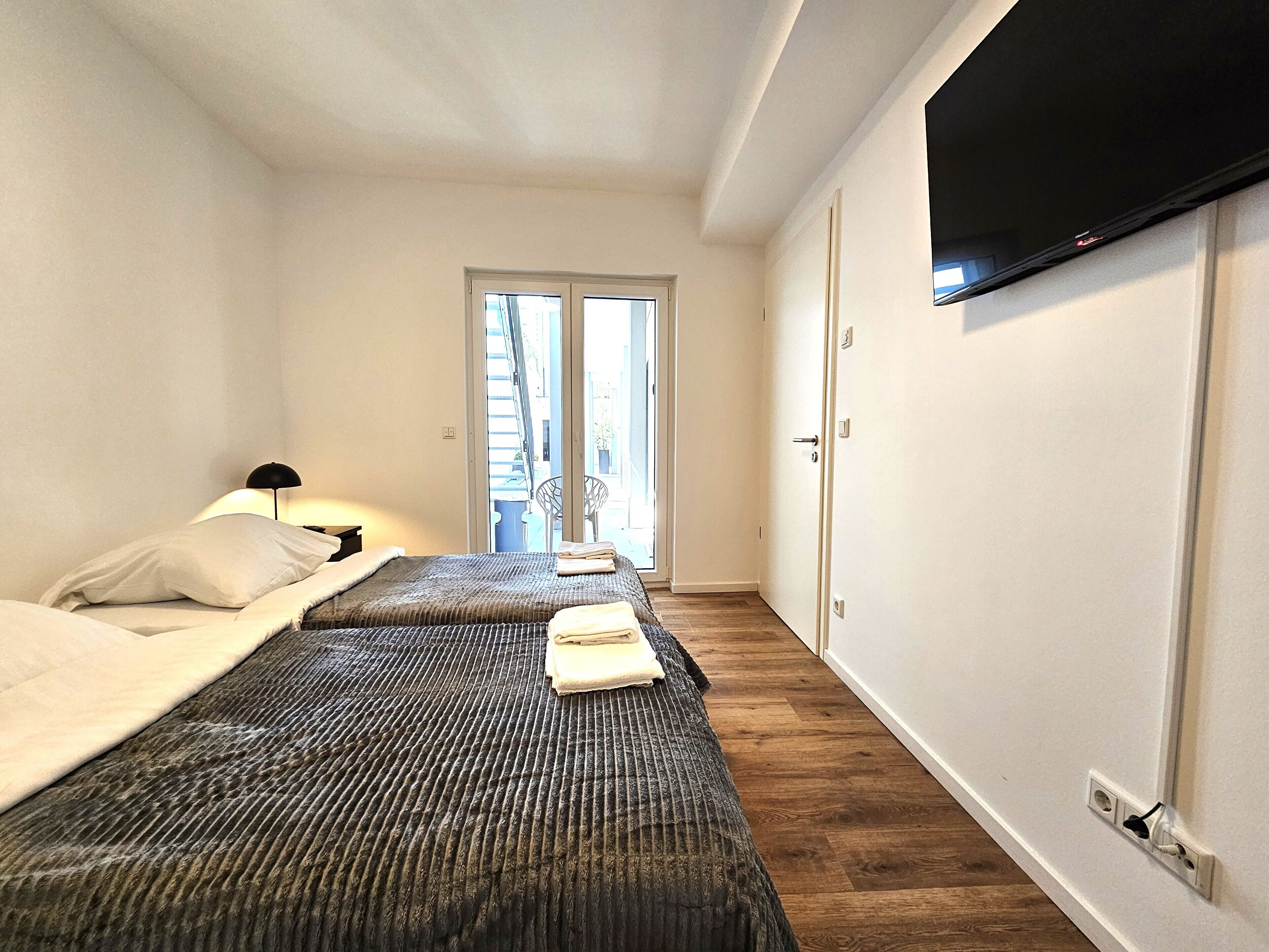 A hotel room with two beds, a TV mounted on the wall, and a door leading to a balcony.