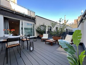 A rooftop patio with a wooden deck, outdoor seating, and potted plants.