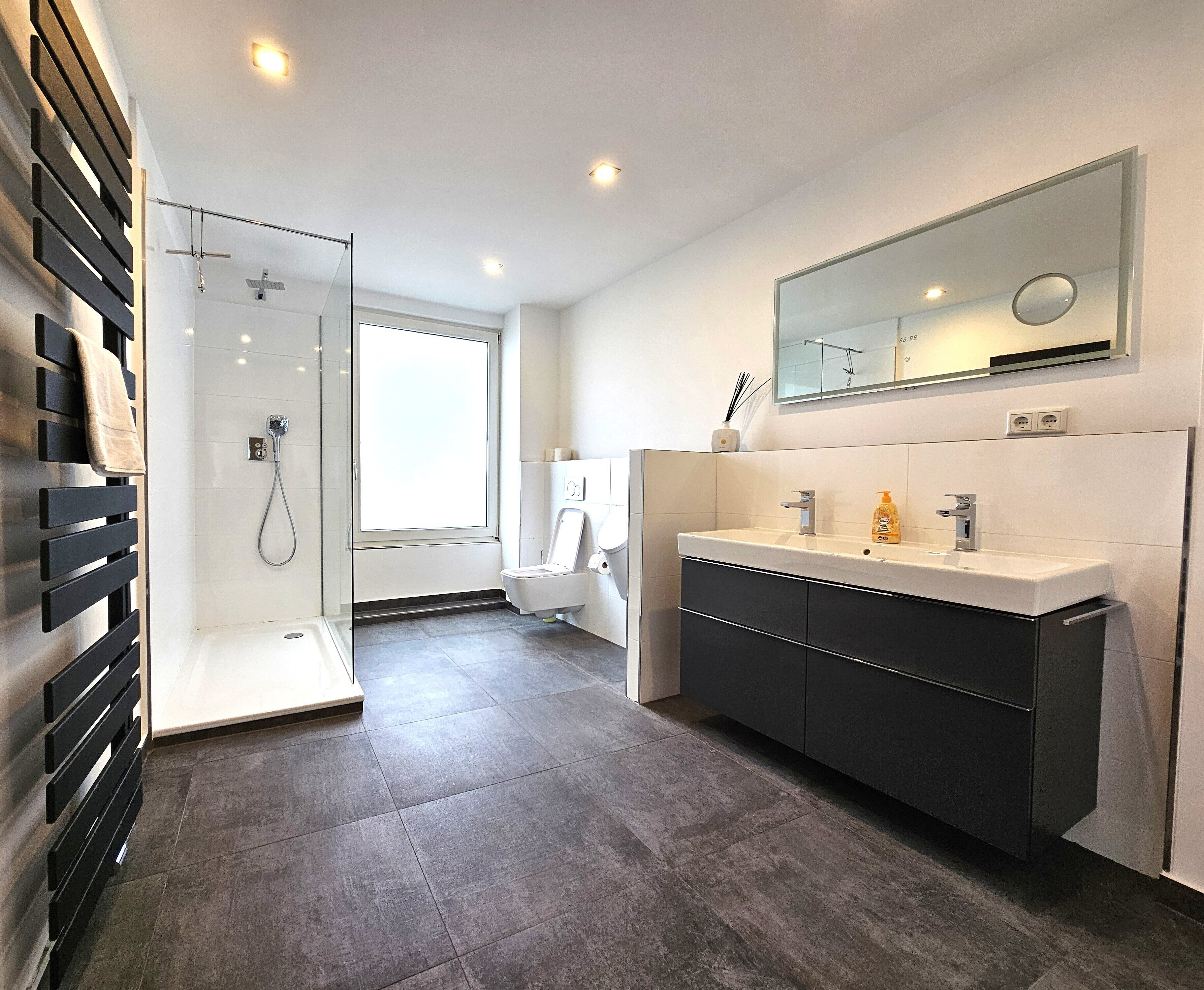 Ein modernes Badezimmer mit barrierefreier Dusche, einem großen Spiegel und einem Waschtisch mit dunklen Schränken.