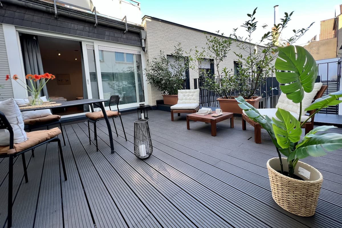 Une terrasse extérieure avec une plateforme en bois, des coins salon et des plantes en pot.