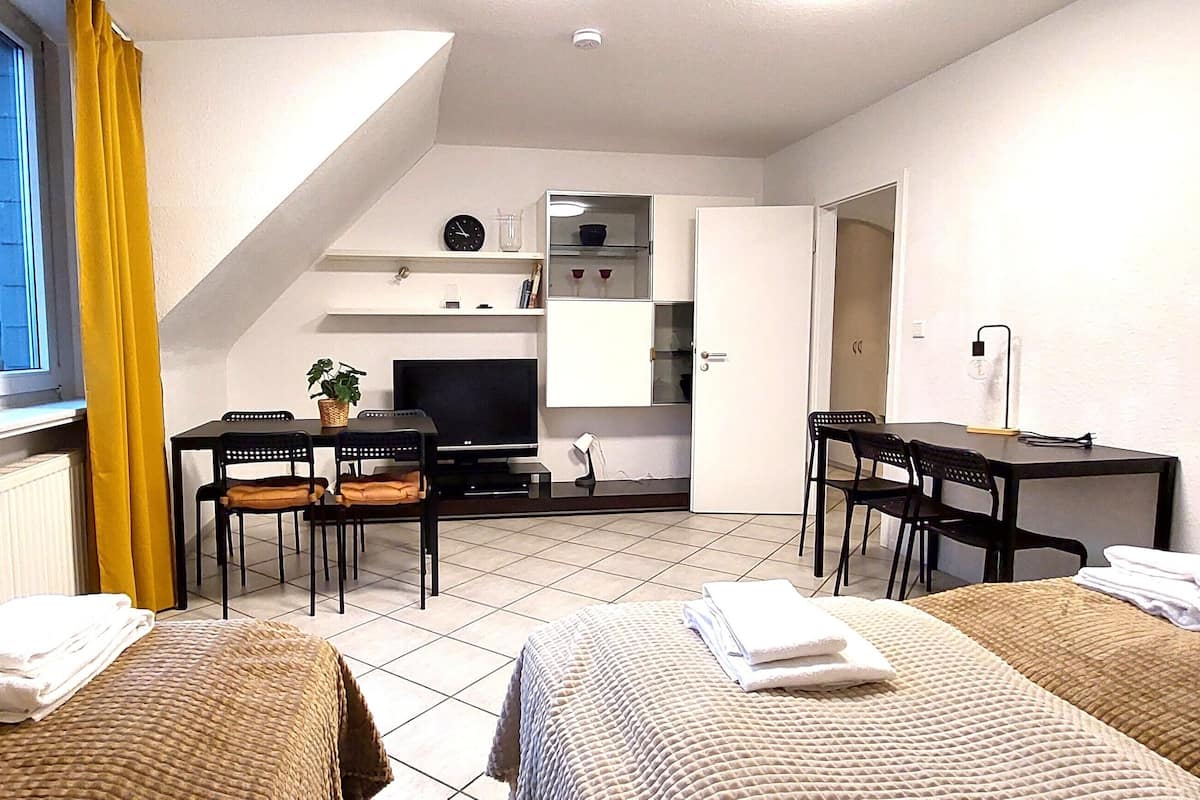 Une chambre d’hôtel compacte comprenant deux lits, un bureau, une chaise, une télévision et une petite kitchenette.