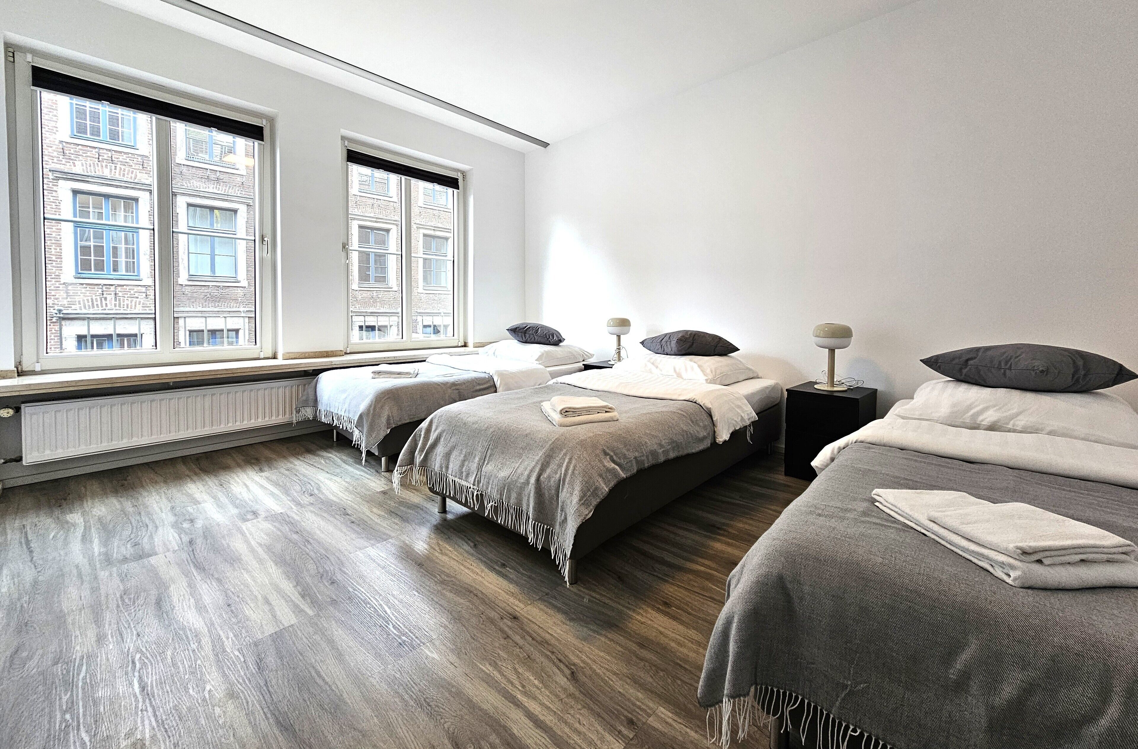 A modern hotel room with two beds, a large window with a city view, and a wooden floor.